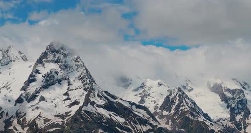 Air Flight Through Mountain Clouds Over Beautiful Snowcapped Peaks of Mountains and Glaciers