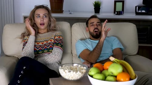 Couple Watching TV on Sofa, Reacting to Program