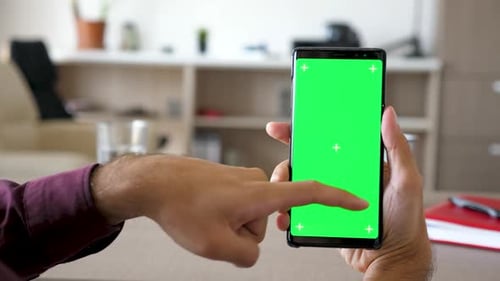 Man Using a Modern Smartphone with Green Screen Chroma Mock-up in His Living Room