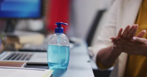 Mid section of woman sanitizing her hands at office