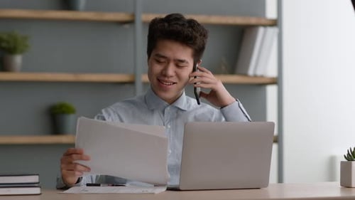 Junger positiver asiatischer Büroleiter schaut sich Dokumente an und spricht mit Geschäftspartnern über