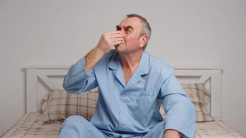 Adult Man Holding Nose on Bed in Bedroom