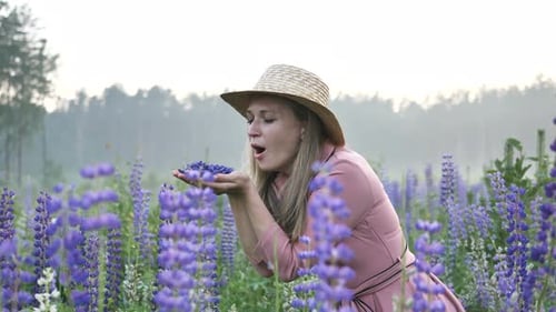 Pretty Woman Blows Petals of Purple Lupin Flowers on Meadow