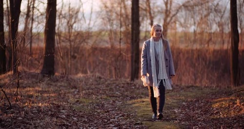 Woman Walking Through Autumn Forest at Sunset