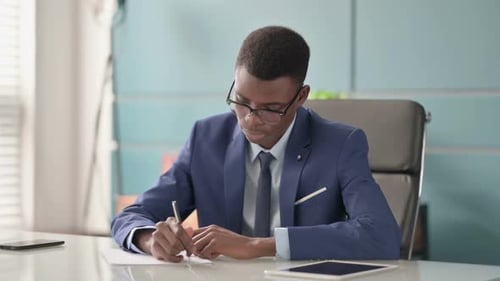 Young African Businessman Writing on Paper in Office