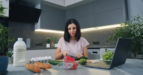 Ama de casa corta pepino para ensalada y ve simultáneamente un programa culinario en línea en la cocina