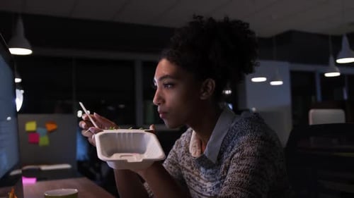 Businesswoman working and eating in a modern office by night