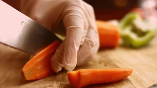 Gloved Hands Cutting Carrots on Cutting Board