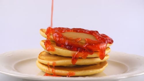 Pouring Strawberry Syrup onto Stack of Pancakes