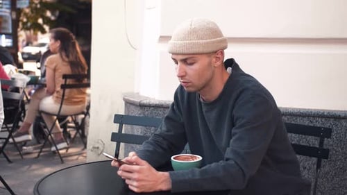 Portrait of Young Caucasian Man Sitting in the Outdoor Cafe and Receiving Bad News on the Phone