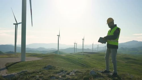 Technician Engineer in Wind Turbine Power Generator Station Standing with a Tablet in His Hands