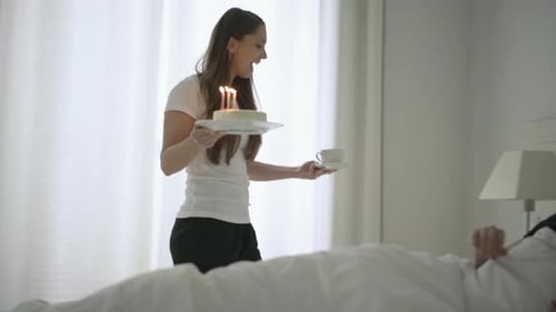 Joven esposa llevando el pastel de cumpleaños de su esposo a la cama