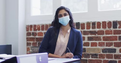 Portrait of woman wearing face mask sitting on her desk at office