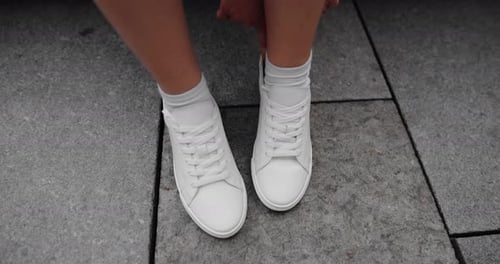 Woman Adjusting White Sneakers on Pavement