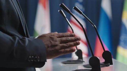 Man Gesturing at Podium with Flags Background