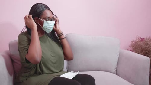 Young african woman wearing face mask, protection covid-19 epidemic in living room.