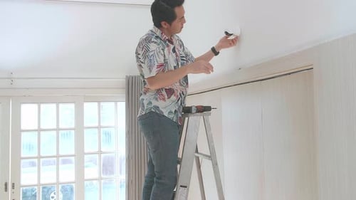 Adult Installs Security Camera on Wall Indoors