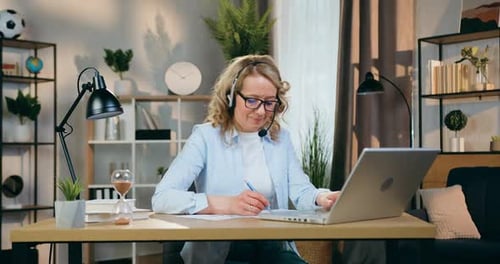 Femme au casque travaillant avec des documents et des informations sur un ordinateur portable sur le lieu de travail dans une pièce confortable