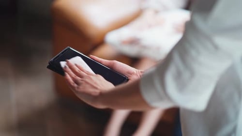 Asian woman holding her phone and cleaning screen by Microfiber cloth at home for prevent bacteria.
