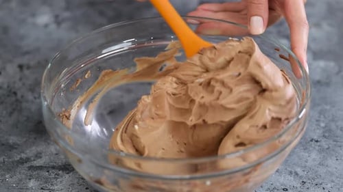 Weibliche Hände rühren Schokoladencreme mit einem Spatel um.