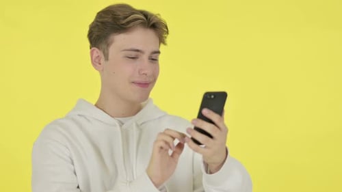 Young Adult Using Smartphone on Yellow Background