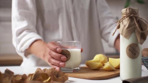 Niña bebe leche vegetal de pie en la cocina, cocinando sin leche a base de papa, sin carne