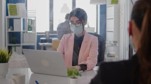 Woman working on laptop in office wearing mask