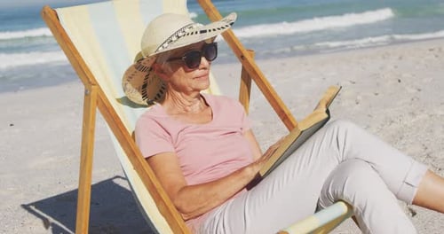 Senior Caucasian woman sitting on sunbeds at the beach.