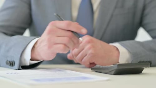 Nahaufnahme eines Geschäftsmannes, der mit einem Taschenrechner auf Papier schreibt