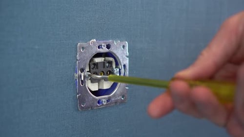 Electrician Repairing a Wall Outlet with a Screwdriver