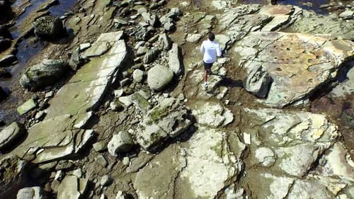 Tracking shot of a young man running on a rocky ocean beach shoreline