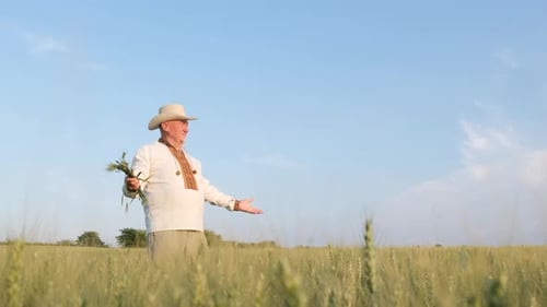 A Joyful and Happy Farmer in the Middle of a Wheat Field Against a Blue Sky