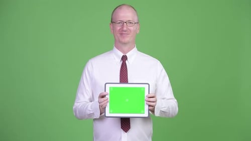 Heureux homme d'affaires chauve mature montrant tablette numérique