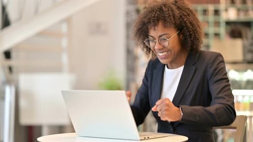 Excited African Businesswoman Celebrating Success on Laptop at Cafe