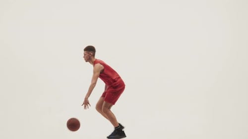 Jeune joueur de basket-ball en uniforme de sport court et dribble sur un fond de studio blanc