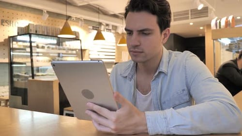 Casual Young Man Using Tablet PC in Cafe