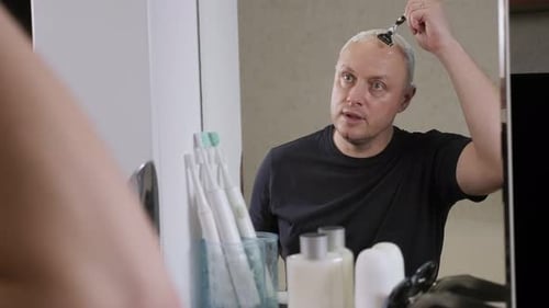 Man Shaves Head in Bathroom Mirror