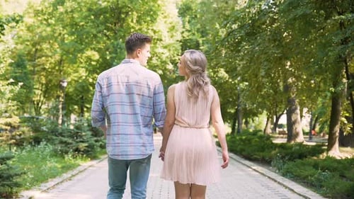 Beautiful young couple slowly strolling through sunlit bright green park, date
