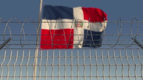 Bandera ondeante de República Dominicana detrás de alambre de púas