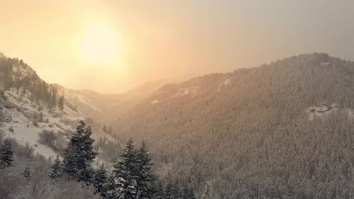 Flying over snowy canyon towards the sun shining through the clouds