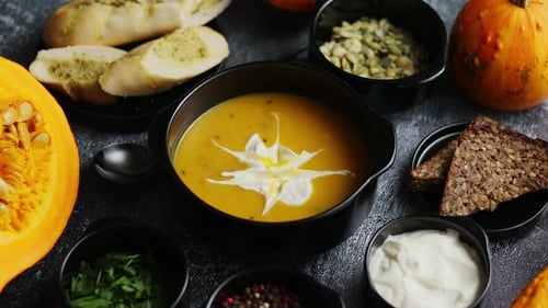 Delicious Pumpkin Soup with Cream, Seeds, Bread and Fresh Herbs in Elegant Ceramic Black Bowl