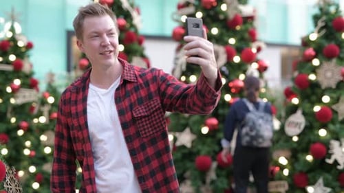 Man Chatting on Video Call Among Christmas Trees