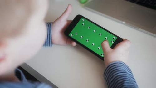 Kid Boy nutzt Smartphone mit grünem Mockup-Bildschirm beim Spielen oder Surfen im Internet auf dem Telefon
