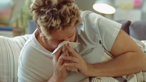 Sick Man Blowing Nose and Taking Medicine in Bed