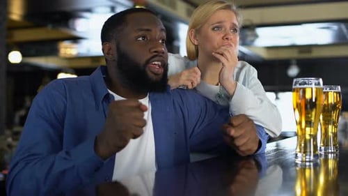 Young Biracial Couple Rooting Favorite Sport Team in Bar, Watching Match Online