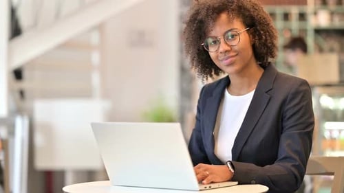 Young African Businesswoman with Laptop Smiling at Camera in Cafe