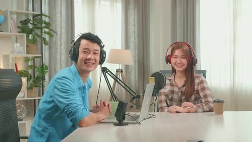 Asian Man Host Record Podcast Wear Headphone With Young Woman Guest Looking And Smiling To Camera