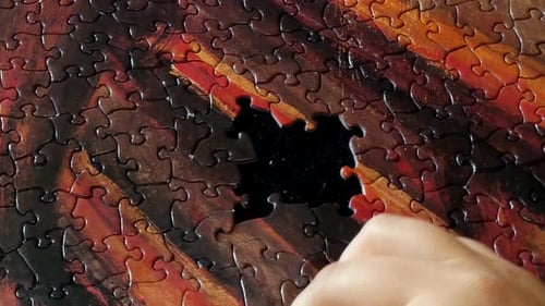 Eine Hand arbeitet an einem farbenfrohen Puzzle.