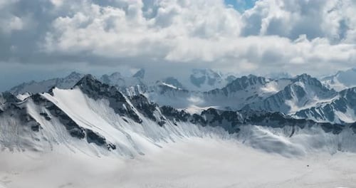 Air Flight Through Mountain Clouds Over Beautiful Snowcapped Peaks of Mountains and Glaciers
