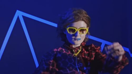 Young Redhead Girl in Sunglasses Fashion Dance on a Black Background That Changes Colors of Light